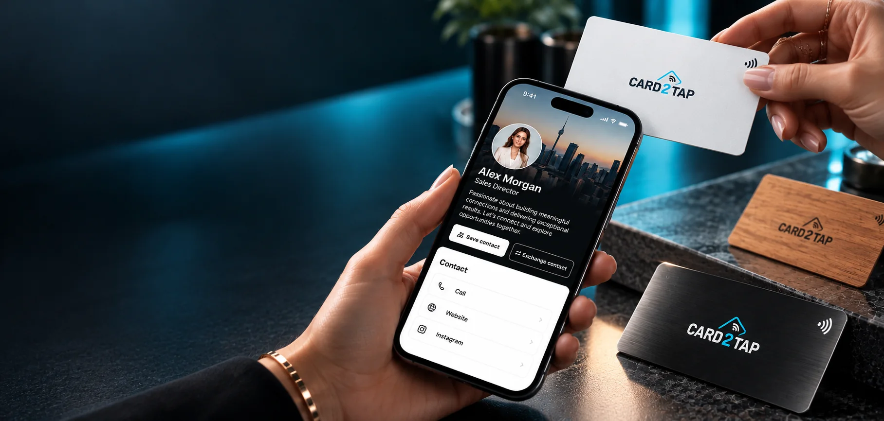 A hand holding a phone with a Card2Tap digital profile under a white Card2Tap card, with wooden and black Card2Tap cards on the counter