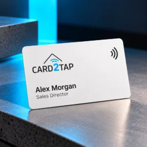 White PVC Card2Tap NFC business card with the Card2Tap logo, the name Alex Morgan and the title Sales Director, on a stone ledge lit in blue